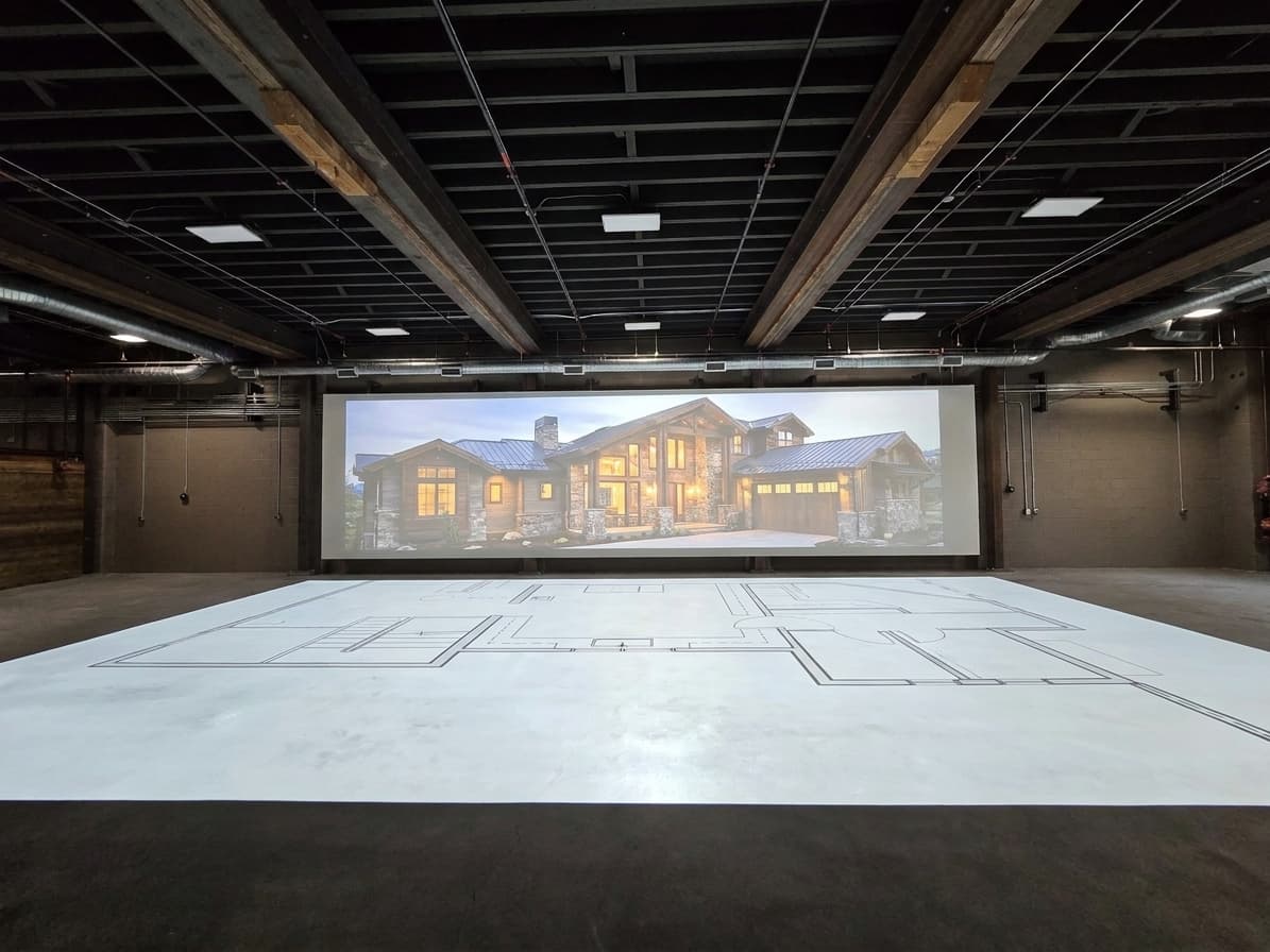 Visitors walking through architectural plans projected across the walls and floor of CDA Immersive Studio